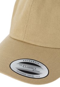 Beige színű baseball sapka ívelt silddel, texturált anyagból, és egy kerek fémlapkával, amelyen az "AUTHENTIC THE CLASSICS YUPOONG SINCE 1974" felirat olvasható.