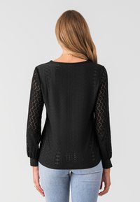 Schwarzes Langarmoberteil mit einem strukturierten Strickdesign und runden sowie diamantförmigen Ausschnitten. Mit einem runden Ausschnitt und enganliegenden Manschetten gestylt.