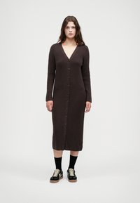Ριγέ καφέ μακριά καρντιγκάν με V-λαιμό, μπροστινά κουμπιά και μακριά μανίκια, σε συνδυασμό με μαύρα παπούτσια και κάλτσες μέχρι το γόνατο.