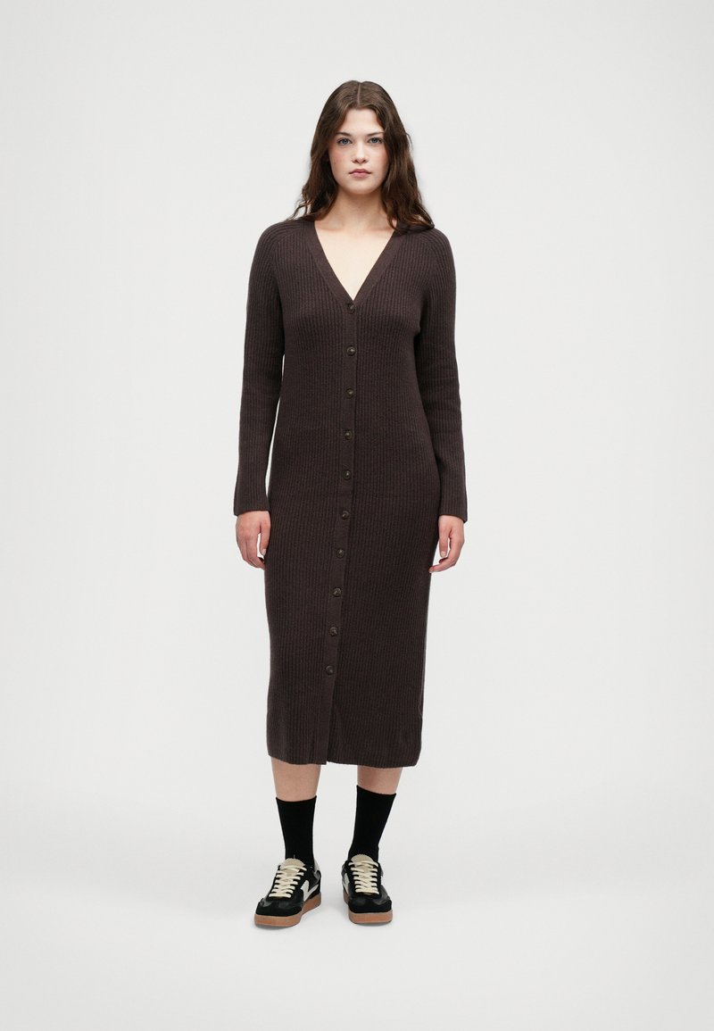 Ριγέ καφέ μακριά καρντιγκάν με V-λαιμό, μπροστινά κουμπιά και μακριά μανίκια, σε συνδυασμό με μαύρα παπούτσια και κάλτσες μέχρι το γόνατο.