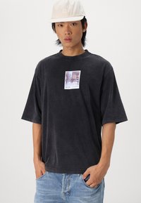 Mørkegrå, oversized T-shirt lavet af blødt bomuld med rund hals og kortærmede, med et fotografisk print på brystet.