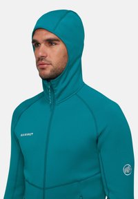 Giacca con cappuccio turchese con chiusura a zip, design aderente, cuciture a contrasto e logo Mammut sul petto e sulla manica.