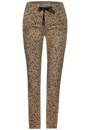 Schmal geschnittene beigefarbene Hose mit schwarzen abstrakten Tigerstreifen und einem schwarzen Kordelzug an der Taille, versehen mit Taschen vorne und hinten.