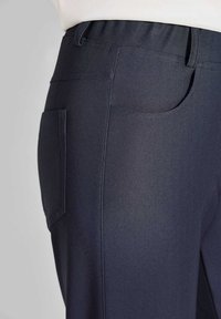 Marineblauwe broek van textuurstof, met een elastische tailleband en zijzak. Het ontwerp heeft een gladde afwerking en een getailleerde pasvorm.