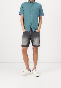 Turkos kortärmad knapplös skjorta med ficka, kombinerad med grå denimshorts med uppvikta ärmar. Vita sneakers med mörka detaljer fulländar looken.