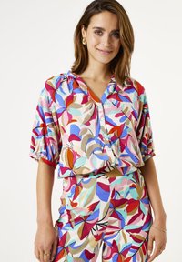 Mehrfarbige Bluse mit V-Ausschnitt, kurzen Ärmeln und Knopfdetails. Sie zeichnet sich durch ein abstraktes Blumenmuster in Pink-, Blau- und Rottönen aus.