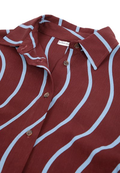 Chemise bordeaux à boutons avec des rayures verticales ondulées bleu clair et un col, partiellement déboutonnée, montrant une petite étiquette de marque à l'intérieur.