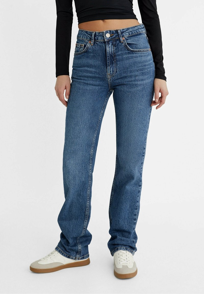 Jeans blu a vita alta con vestibilità dritta, realizzati in tessuto denim. Presentano cinque tasche e una leggera scoloritura. Abbinati a sneakers bianche.