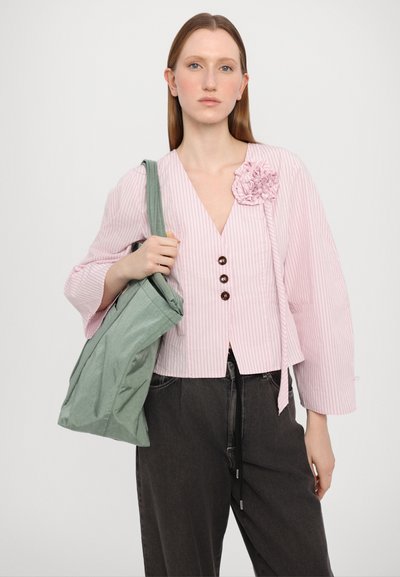 Giacca cropped a righe rosa con tre bottoni marroni e un dettaglio in tessuto a forma di fiore, abbinata a pantaloni grigi larghi e una borsa a tracolla verde.
