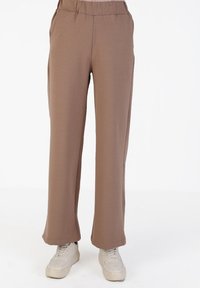 Bruine wijde broek gemaakt van zachte stof met een elastische tailleband en zijzakken, gecombineerd met lichtgekleurde schoenen.
