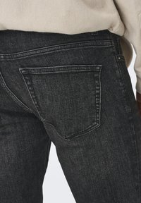 Blugi negri din denim cu o croială slim, având un buzunar la spate și cusături în contrast. Textura este netedă, cu un aspect ușor decolorat.