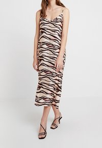 Satin midi-mekko, jossa on V-pääntie ja aaltoileva ruskea ja punainen kuvio kermanvärisellä taustalla; ohuet spagettiolkaimet; sileä rakenne.