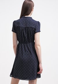 Marinblå klänning knälängd i lätt tyg, med vita prickar, korta ärmar och detaljer med elastisk midja.