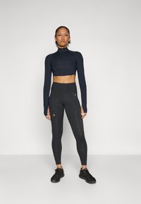 Zwarte cropped lange mouwen top met een hoge kraag, gecombineerd met hoge taille zwarte leggings met een discreet logo. Beide zijn gemaakt van rekbare stof.