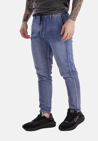 Pantaloni jogger in denim azzurro chiaro con vestibilità affusolata, cintura con cordino e dettagli sbiaditi. Abbinati a sneaker sportive nere.