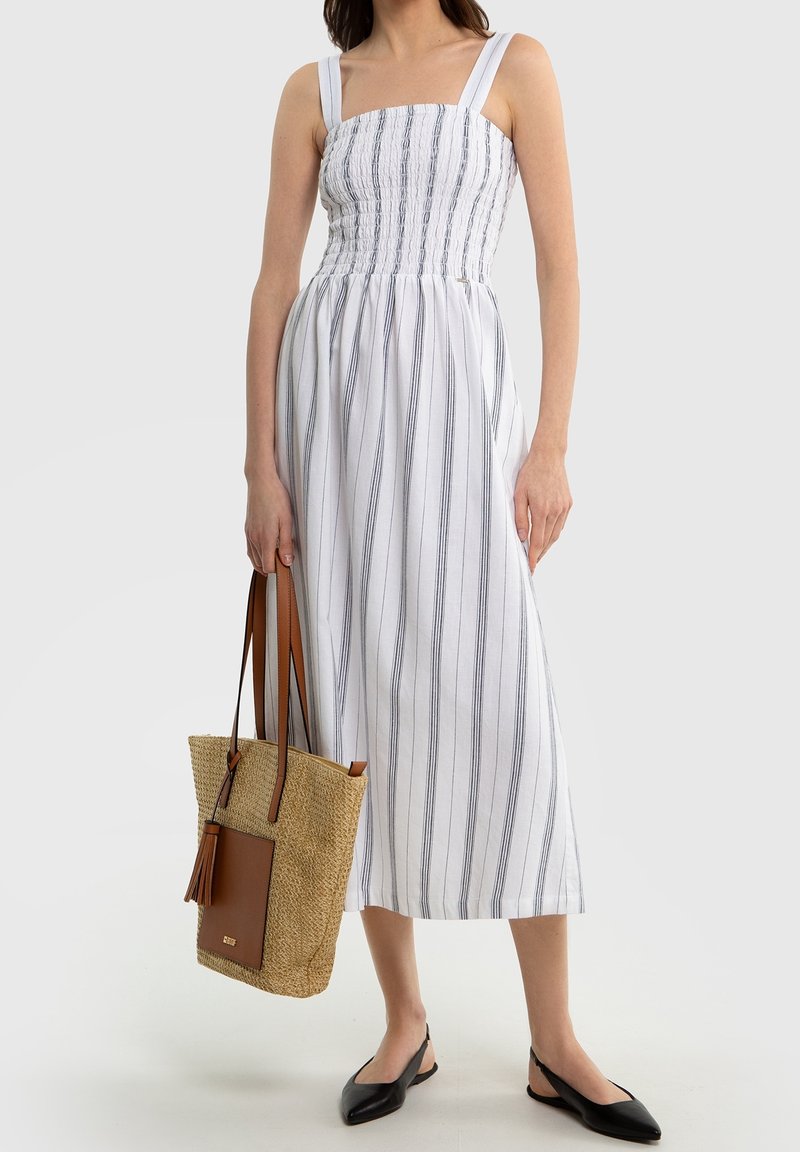 Valkoisiraidallinen mekko, jossa on leveät olkaimet, istuva yläosa ja valuva helma. Sen mukana tulee kudottu olkalaukku ja mustat avokas-tyyliset kengät.