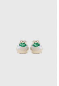 Hvite lær sneakers med grønne detaljer, beige semsket skinn og en fremtredende grønn "VEJA"-logo på hælen, med en teksturert gummisåle.