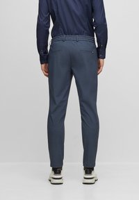 Marinblå skräddarsydda byxor med en strukturerad yta, elastisk midja och två bakfickor. Matchas med vita och svarta sneakers.