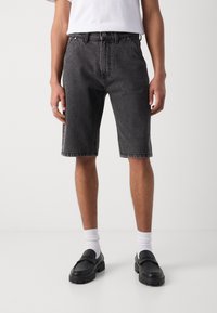 Svarta jeansshorts med avslappnad passform, med knapp- och dragkedjestängning, framfickor och nedvikta fållar. Bärs med vita strumpor och loafers.