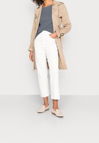 Beige trench coat yli tummansinisen ja valkoisen raidallisen paidan, yhdistettynä valkoisiin lyhennettuihin housuihin ja vaalean värisiin loafer-kengiin. Sujuvat pinnat ja klassinen muotoilu.