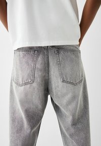Verbleekte grijze denim jeans met een rechte snit, voorzien van twee achterzakken en subtiele slijtagepatronen, gecombineerd met een eenvoudig wit shirt.