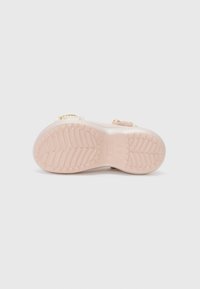 Semelle d'une sandale rose clair avec un motif de sculpture texturé et une petite boucle, présentée sur un fond neutre.