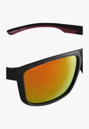 Čierne slnečné okuliare s reflektívnymi šošovkami v oranžovo-zelenom odtieni. Matný povrch a mierne zakrivený rám. Poznámka: "KOMERČNÝ VZORKA" na nožičke.
