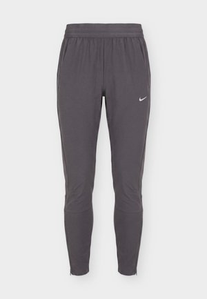 Ciemnoszare, zwężane spodnie sportowe z elastycznym pasem, bocznymi kieszeniami, subtelnymi szwami na kolanach i małym białym logo Nike na prawej udzie.