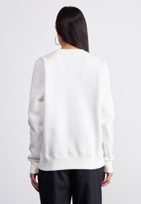 Λευκή μπλούζα με κολάρο crew, μακριά μανίκια και χαλαρή εφαρμογή. Διαθέτει ριμπ μανσέτες και στρίφωμα, κατασκευασμένη από απαλό βαμβακερό υλικό.