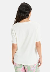 T-shirt blanche à manches courtes avec une coupe ample, un encolure arrondie et des poignets de manches roulés, associé à un pantalon pastel à motifs. Texture lisse.
