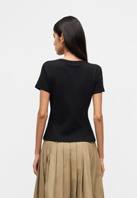 Μαύρο κοντομάνικο T-shirt με στρογγυλή λαιμόκοψη, εφαρμοστή γραμμή και μαλακό ύφασμα. Φορεμένο με ταμπά πλισέ φούστα.