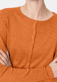 Oranger Cardigan mit runder Ausschnittform, ausgestattet mit einer Knopfleiste vorne und langen Ärmeln aus einem strukturierten Stoff.