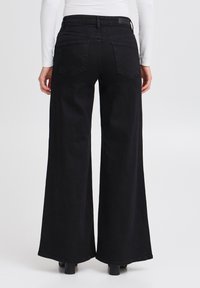 Jeans neri a gamba larga realizzati in denim, dotati di un alto punto vita e due tasche posteriori. L'orlo è rifinito con un bordo pulito.