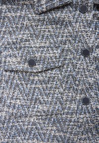 Texturerat tyg i ett fiskbensmönster med blå och vita trådar. Har en bröstficka med en mörk knappstängning.