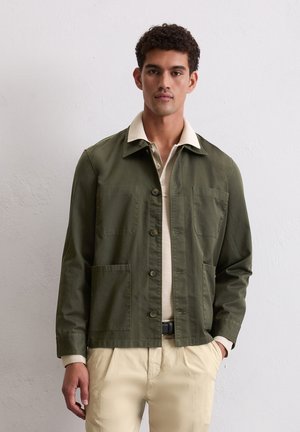 Olive green jacket with a button closure, two front patch pockets, and a contrasting beige collar, worn over a light-colored shirt.