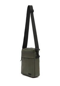 Kompaktna maslinasto zelena crossbody torba s crnim podesivim remenom i zatvaranjem na patentni zatvarač, kutni prikaz na bijeloj pozadini.