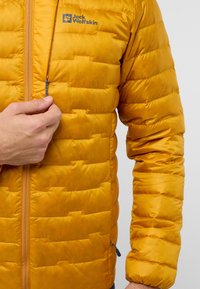 Veste doudoune isolée jaune avec zip sur le devant, texture matelassée et détail du logo. Comprend un col montant et des poches latérales.