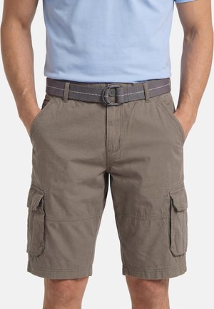 Mann trägt graue Cargo-Shorts mit Seitentaschen und einem grauen Stoffgürtel, Hände in den Taschen, hellblaues Hemd eingesteckt.