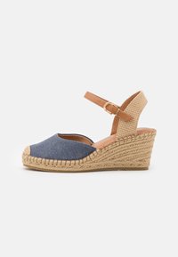 Sandal de cuña de esparto de denim azul con una correa de tobillo trenzada en tono marrón claro, suela de cuerda de yute y diseño de punta redonda. Acentos en cuero marrón claro.