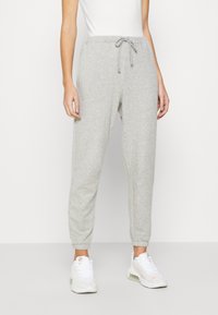 Harmaat collegehousut, joissa on nauhavyötärö, elastiset nilkkahihnat ja pehmeä rakenne. Yhdistetty valkoisiin urheilukenkiin.