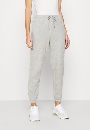 Grijze trainingsbroek met een trekkoord in de taille, elastische enkelboorden en een zachte textuur. Gepaard met witte sportschoenen.