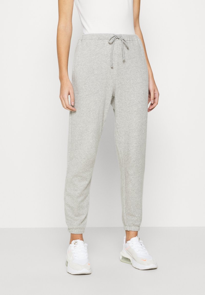 Harmaat collegehousut, joissa on nauhavyötärö, elastiset nilkkahihnat ja pehmeä rakenne. Yhdistetty valkoisiin urheilukenkiin.