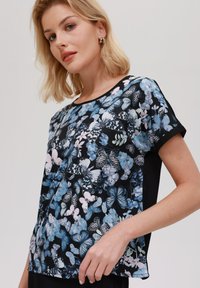 Top con stampa floreale caratterizzata da farfalle e fiori in tonalità di blu e rosa su uno sfondo nero; maniche corte e scollatura rotonda.