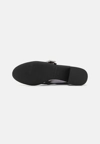 Black flat shoe with textured rubber sole, mesh detailing, and decorative ribbon accent. Features a cushioned insole for comfort.