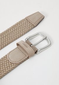 Beige fletet bælte med en glat læderender og en sølvfarvet metalspænde, der har en diskret logodetalje på læderremmen.