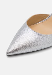 Chaussure à talon aiguille argentée pailletée avec un bout pointu et des côtés ouverts, dotée d'une doublure intérieure lisse et d'une semelle noire élégante.