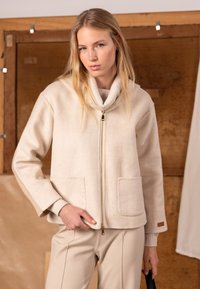 Beige jacka i ullblandning med sjalkrage, dragkedja och framfickor. Ärmarna har ribbade detaljer och en mjuk textur.