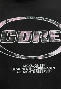 Schwarzes Baumwoll-T-Shirt mit einem großen, verwaschenen weißen "CORE"-Logo und einem rosa Akzent sowie kleineren Text darunter. Einfaches Rundhalsdesign.