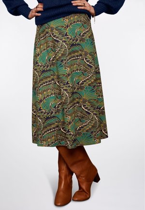 Flared midinederdel med et grønt og gyldent bladmønster på en mørk baggrund. Bæres med knælange brune læderstøvler. Blød stoftekstur.