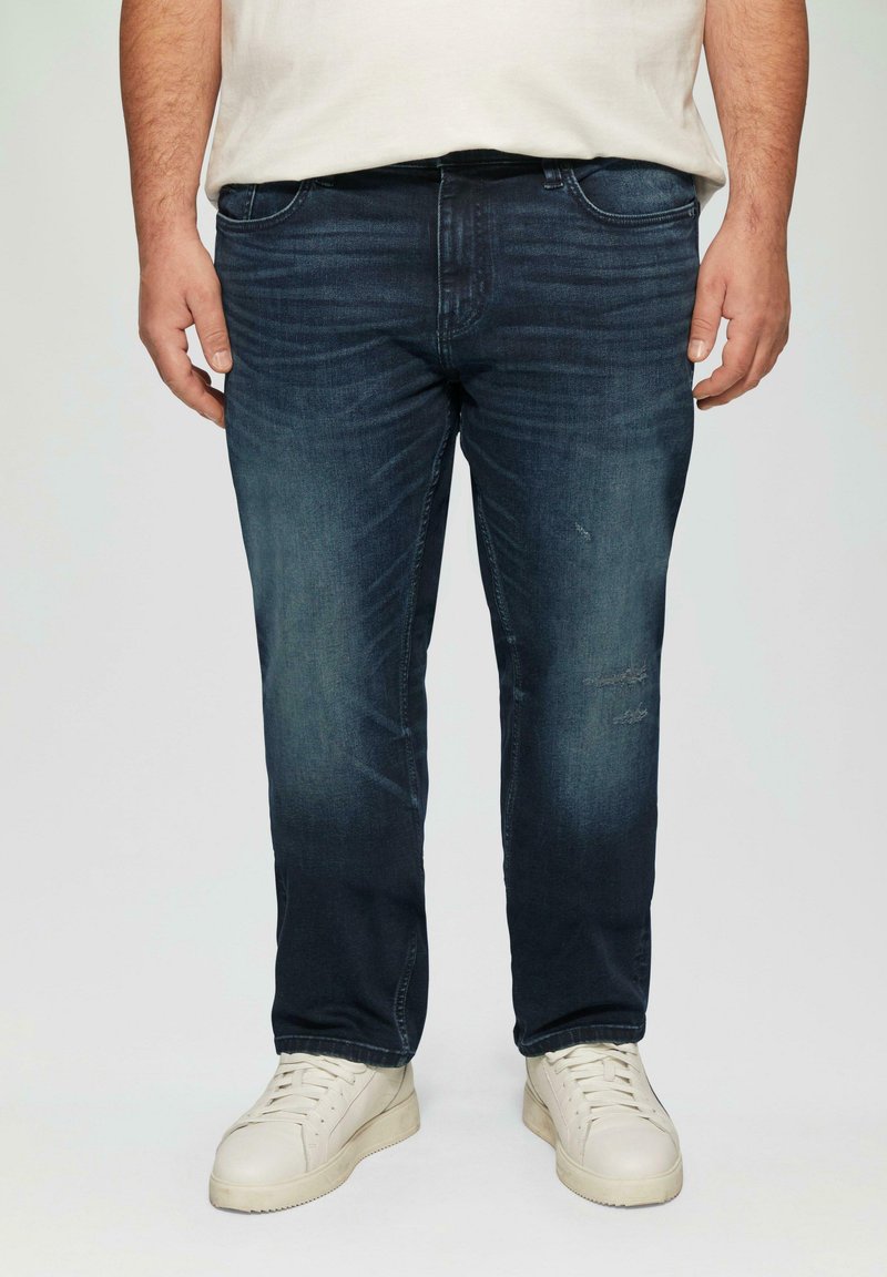 Donkerblauwe denim jeans met een rechte snit, lichte vervaging en kleine slijtage details. Gepaard met witte high-top sneakers.